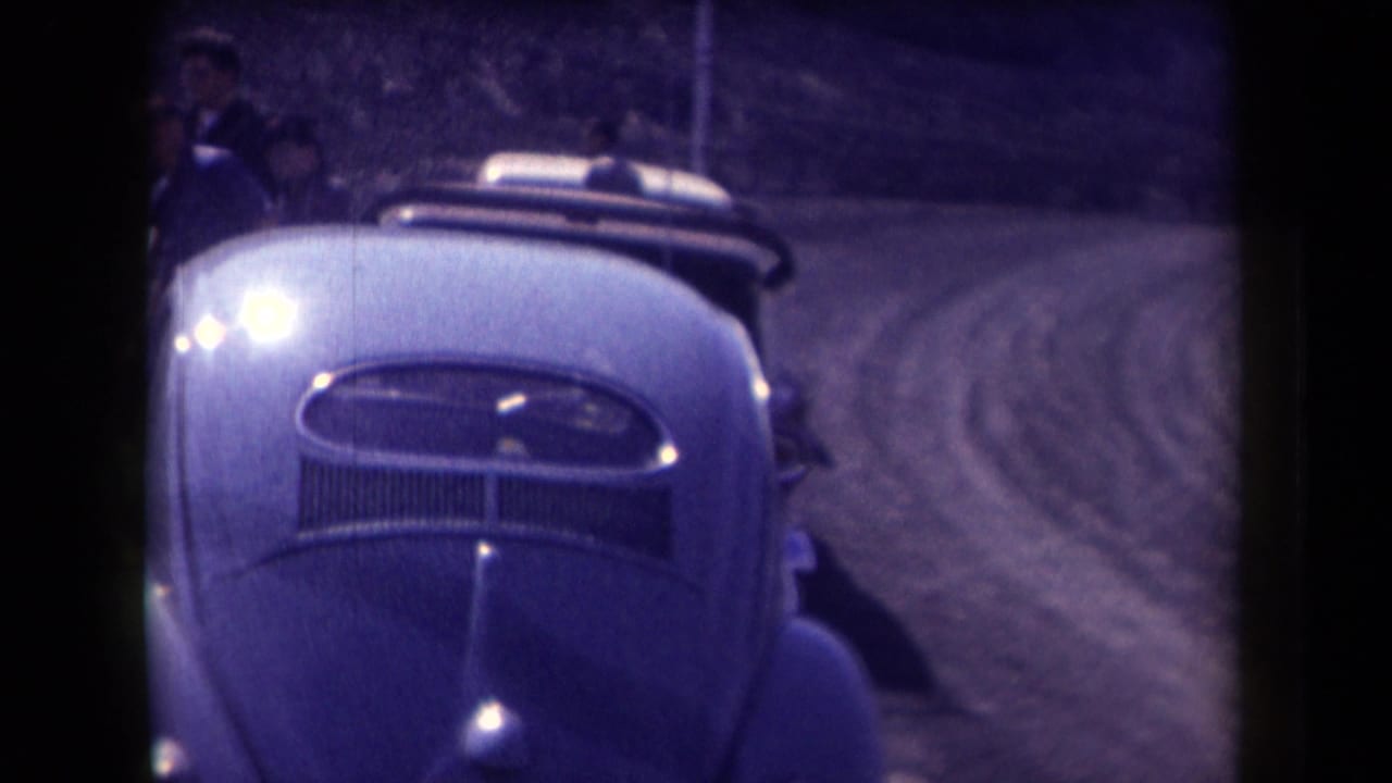 1958 Arizona home-movie frame showing the front of a light-colored Volkswagen Beetle on a curving dirt road in bright sun.