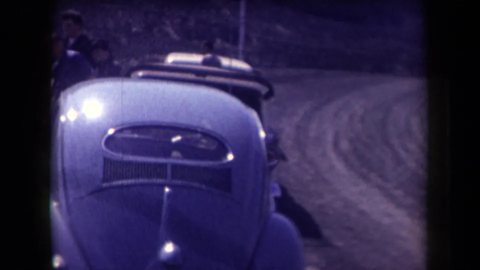 1958 Arizona home-movie frame showing the front of a light-colored Volkswagen Beetle on a curving dirt road in bright sun.
