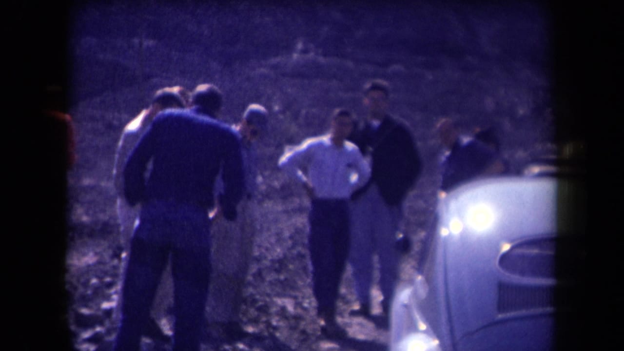 In 1958 Arizona footage, several men gather on a dusty roadside near a light-colored mid-century car.