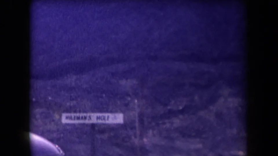 A roadside sign reading HILEMAN'S HOLE appears in sparse Arizona terrain, tinted purple by the 8mm film scan.