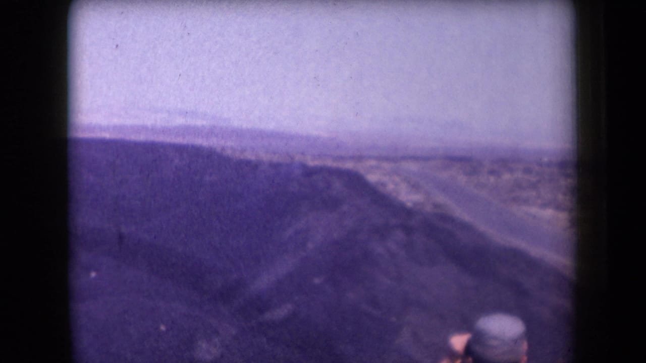 1958 Arizona frame of a broad canyon view and desert road, with a partially visible person in a hat at the lower edge.