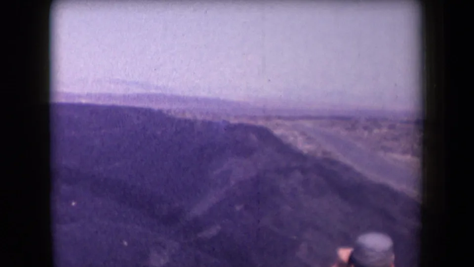 1958 Arizona 8mm frame showing a canyon overlook and winding highway, with a cropped traveler barely visible at the bottom edge.