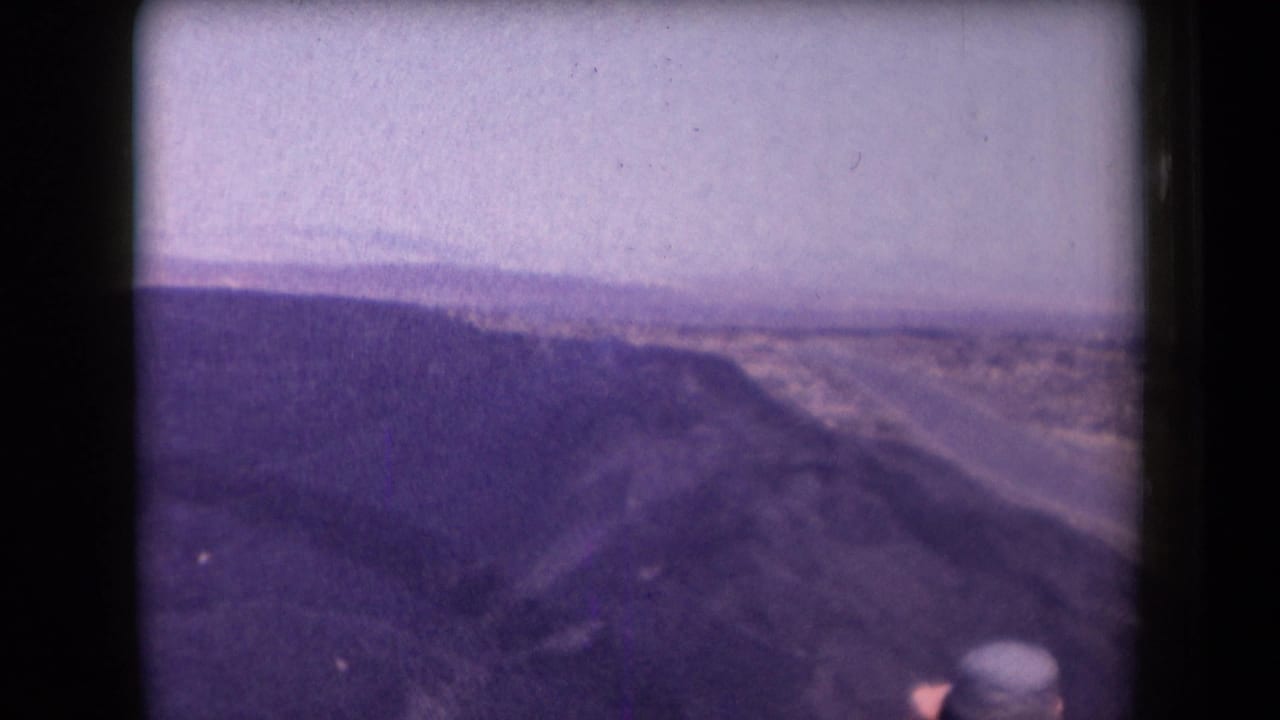 Wide desert view with a partial person in a hat watching from the foreground edge.
