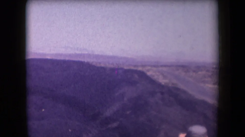 Soft 8mm frame from Arizona in 1958 showing desert terrain, a hazy sky, and a partial foreground observer in a hat.