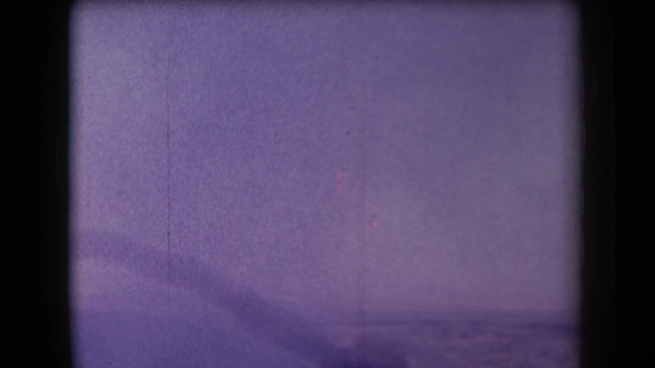 1958 Arizona 8mm frame with a purple cast, soft sky or steam, distant landscape, and dark gate-edge shadows.