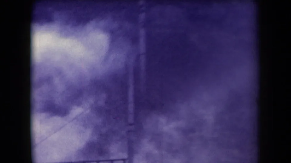 Late frame from the 1958 Arizona 8mm clip showing mist, railing lines, and a vertical post through heavy grain and purple color shift.