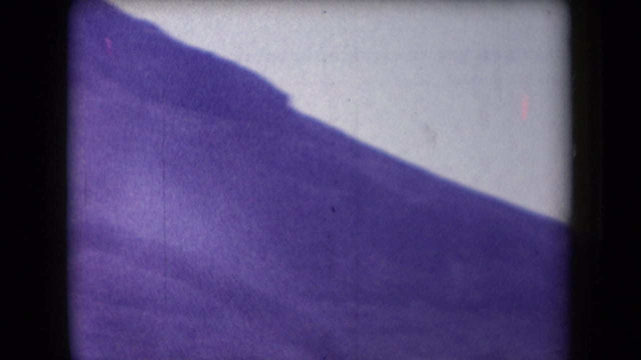 1958 Arizona 8mm frame showing a hazy, purple-cast mountain slope with heavy gate edges and soft exposure.