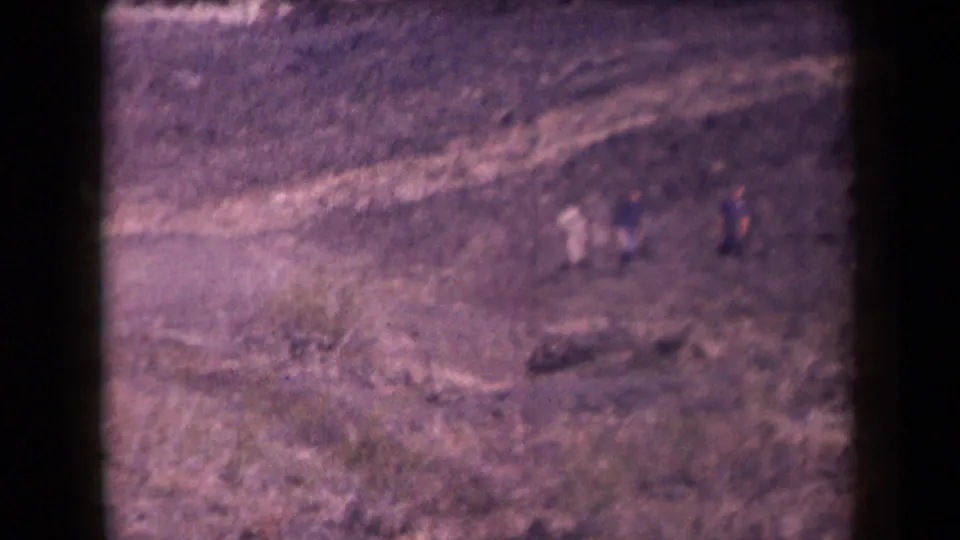 Several distant figures appear on a dusty Arizona slope, recorded from far away on color-shifted 8mm film.