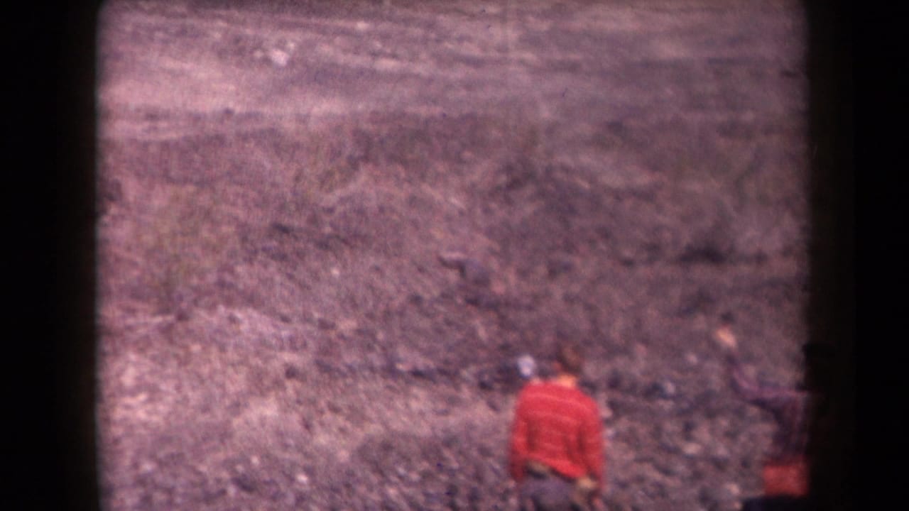 1958 Arizona home-movie frame showing a person in red on rocky desert terrain, with soft focus and dark film edges.