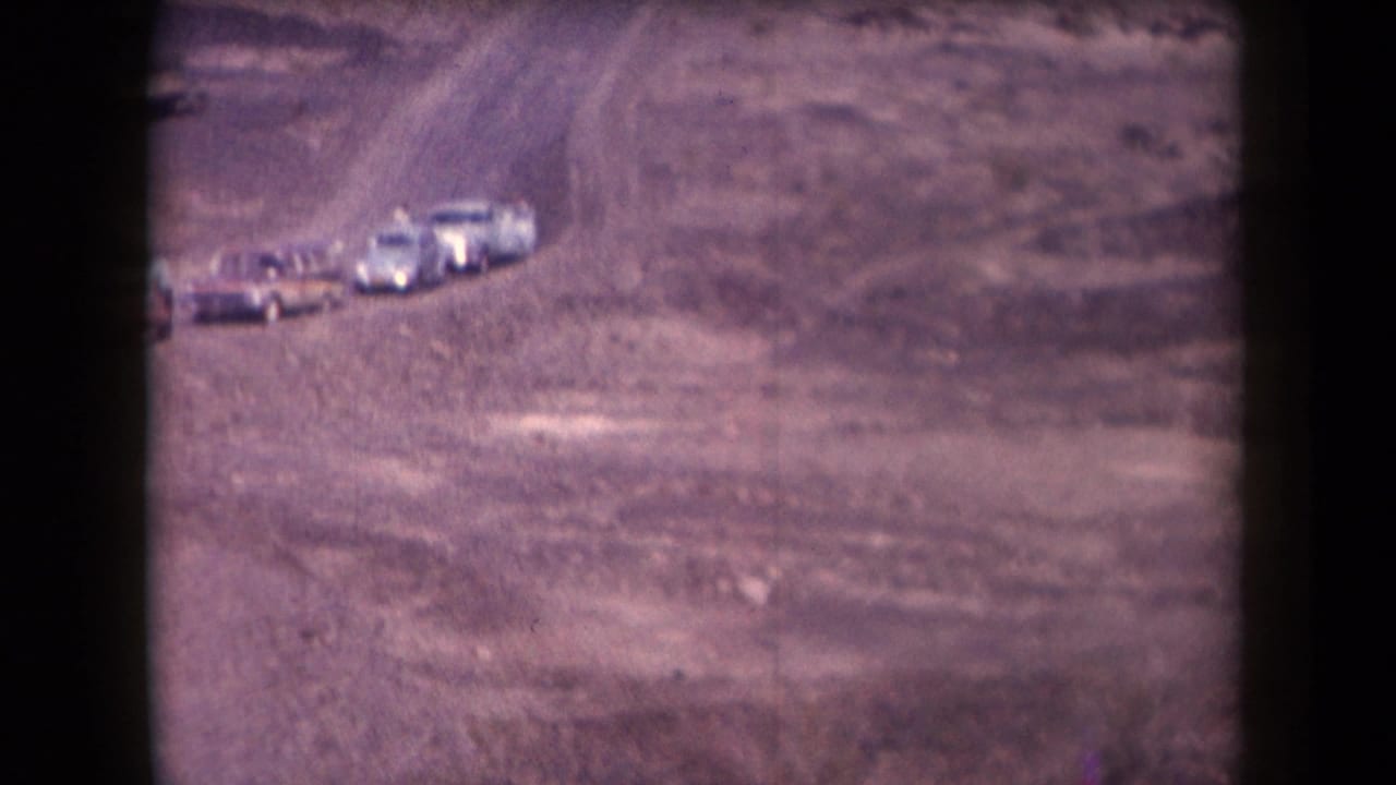Several vintage cars on a dirt road in open desert terrain.