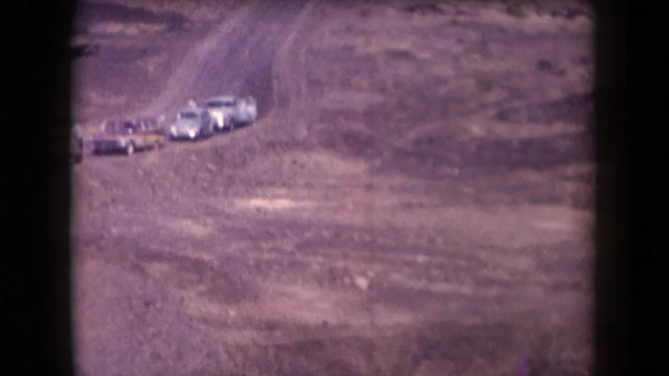 1958 Arizona frame with mid-century cars gathered on a dusty road across a rocky desert landscape.