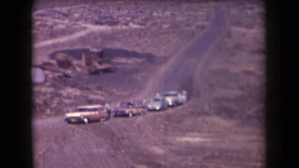 1958 Arizona home-movie view of cars, including a station wagon, near a winding dirt road in rocky desert country.