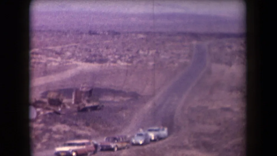 1958 Arizona frame showing a row of vintage cars below a curving dirt road, with open desert stretching into the distance.