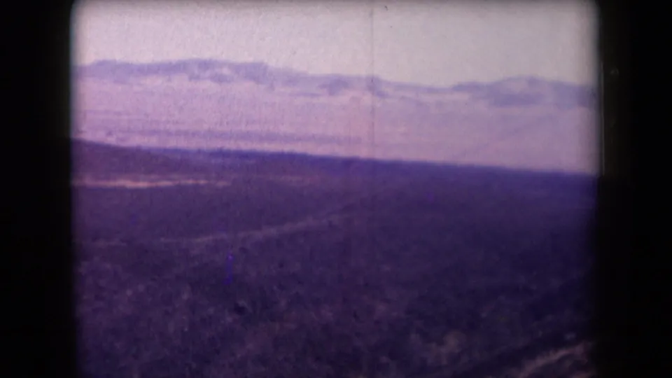 Faded 8mm view of Arizona desert flats and distant hills, framed from a roadside or elevated vantage.