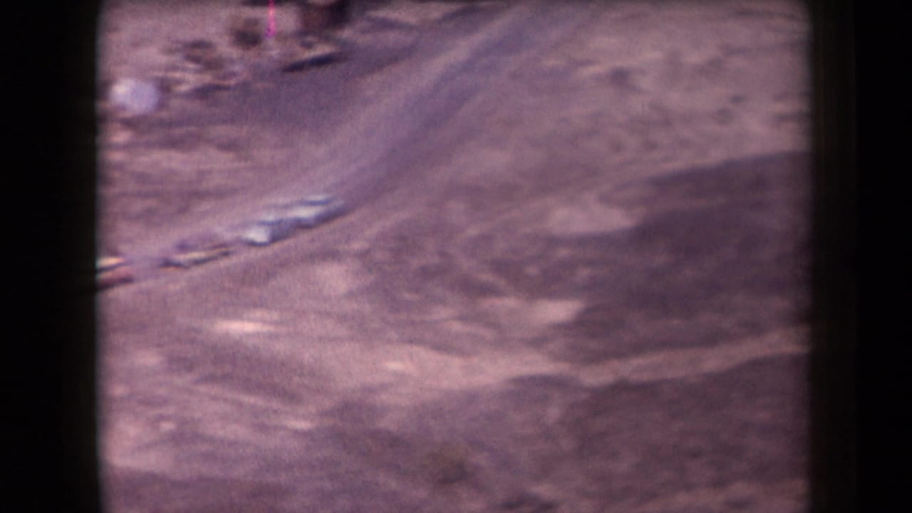 Winding dirt road crosses a barren desert slope with a few small cars.