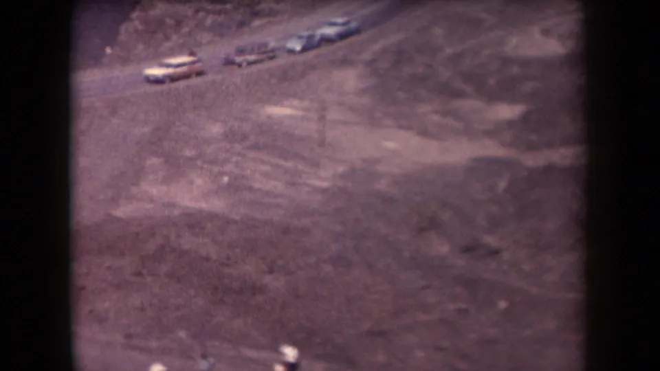1958 Arizona home-movie frame with several light-colored cars on a dusty road across barren terrain.