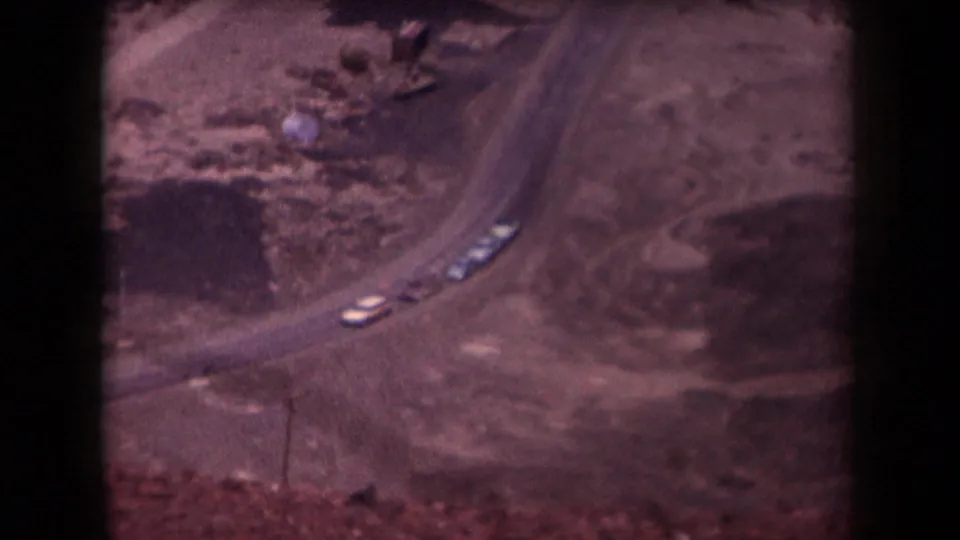 Elevated 1958 Arizona view of a curving road with small cars crossing a dry, cleared-looking landscape.