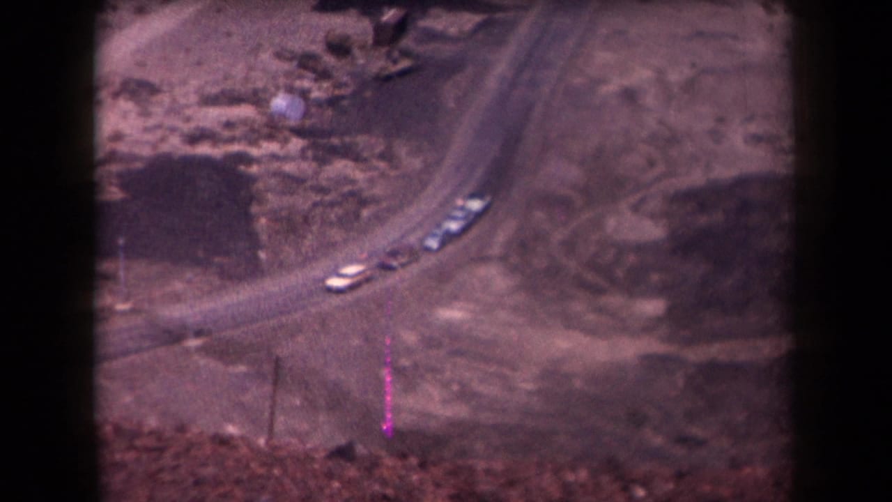 1958 Arizona 8mm frame showing several cars on a curved dirt road through rocky desert ground.