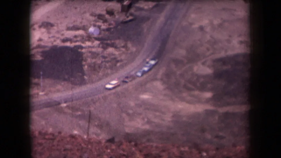 High-angle 1958 Arizona view of light-colored cars moving along a dusty road in open desert terrain.