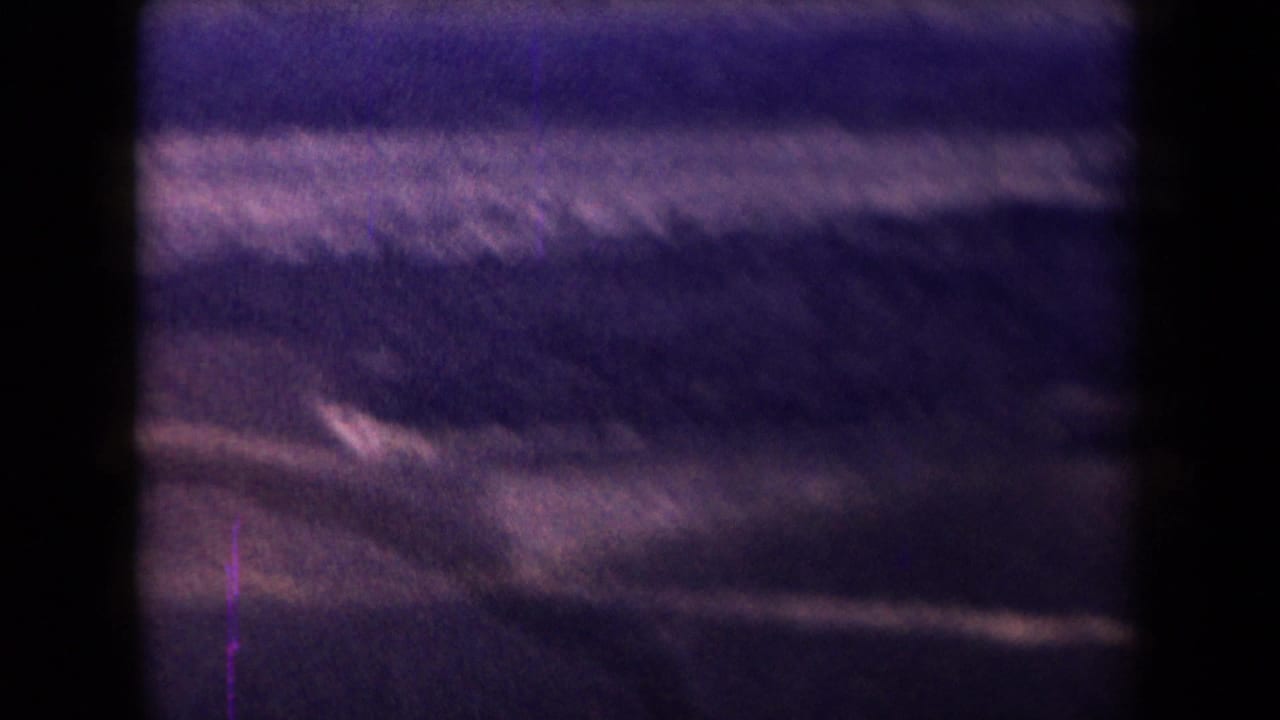 1958 Arizona 8mm frame showing a barren desert view with low rocky slopes, sand, haze, and heavy purple film cast.