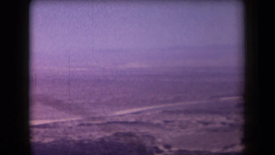 A soft 1958 Arizona 8mm frame shows open sandy desert, faint horizon lines, and a pale sky with strong age-related color shift.