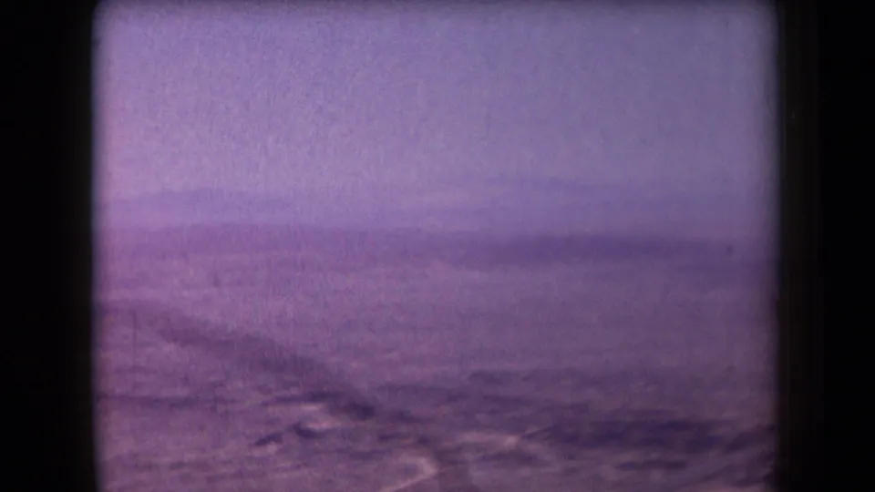 Final sampled frame from 1958 Arizona footage showing barren desert flats, distant slopes, haze, and heavy 8mm color fading.