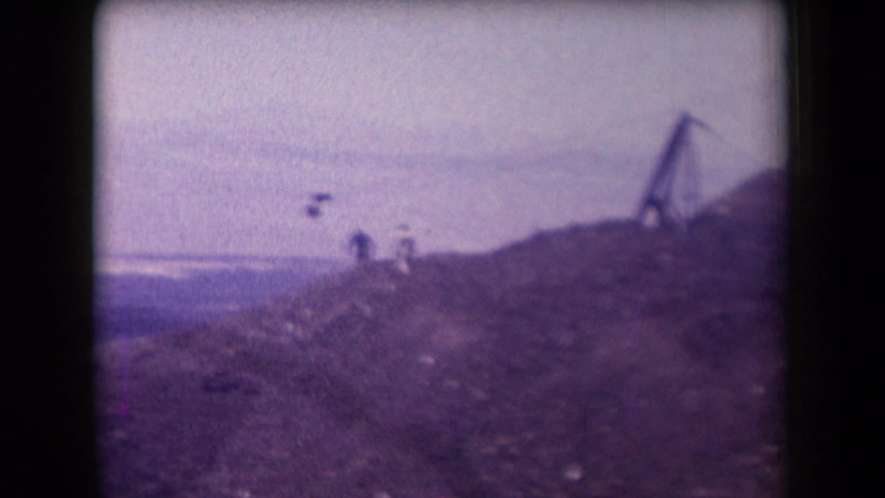 1958 Arizona 8mm frame showing distant people on a rocky desert hill near a simple zipline structure under a hazy sky.
