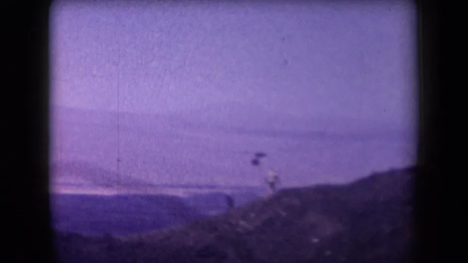 1958 Arizona home-movie frame showing a distant person and zipline line on a ridge above hazy open terrain.