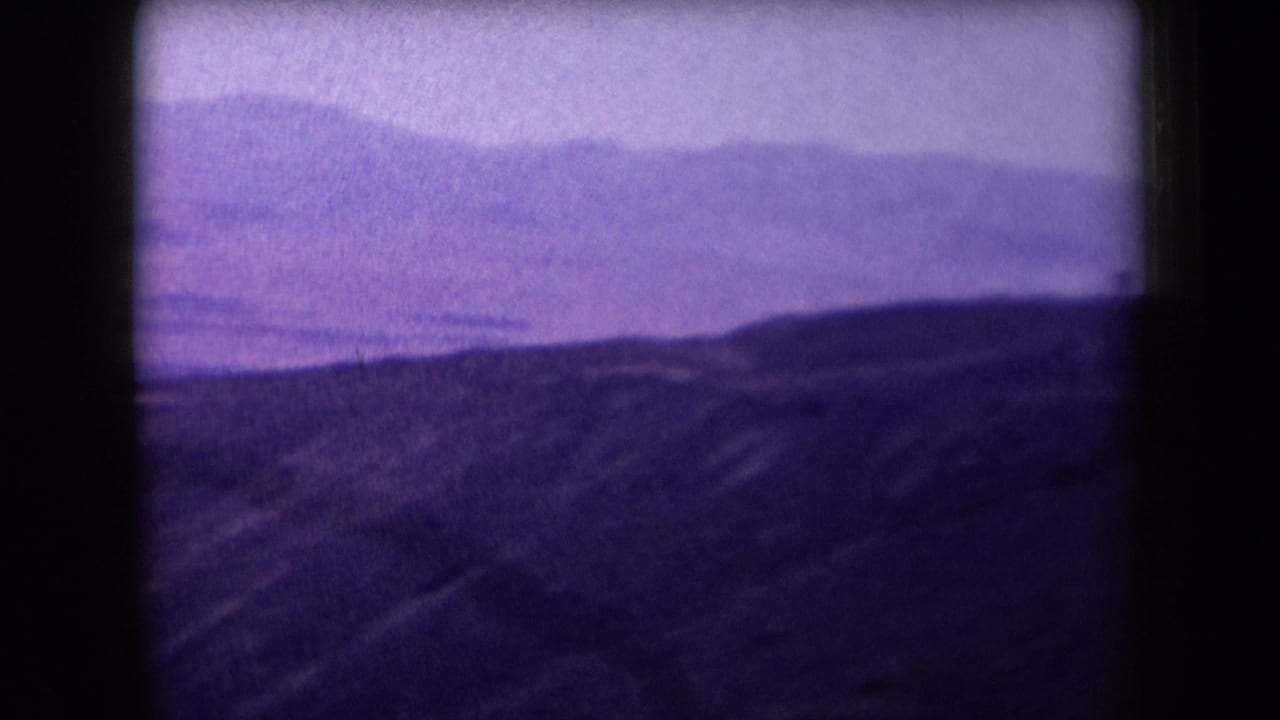 Soft purple view of rolling hills and distant mountain ridges under a bright sky.