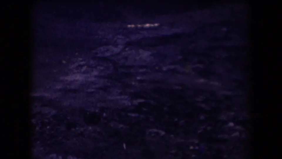 1958 Arizona 8mm frame showing a dim textured foreground, possible rocky ground, faint glints of light, and heavy vignetted film edges.