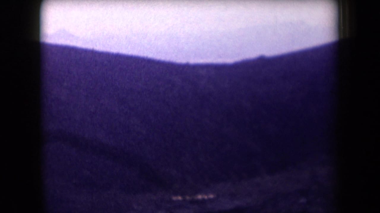 1958 Arizona aerial frame with a distant mountain ridge under a pale hazy sky, bordered by the dark edge of an airplane window.