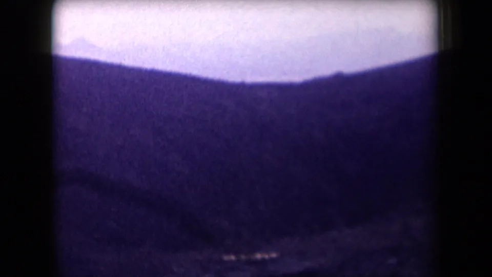 1958 Arizona aerial frame with a distant mountain ridge under a pale hazy sky, bordered by the dark edge of an airplane window.