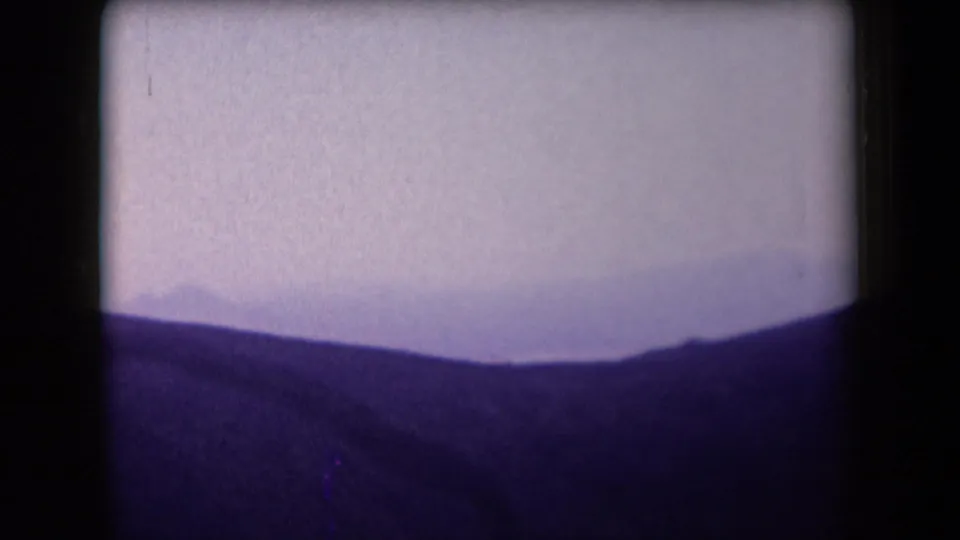 1958 Arizona 8mm frame showing low mountain silhouettes and a pale overcast sky from an aircraft passenger viewpoint.