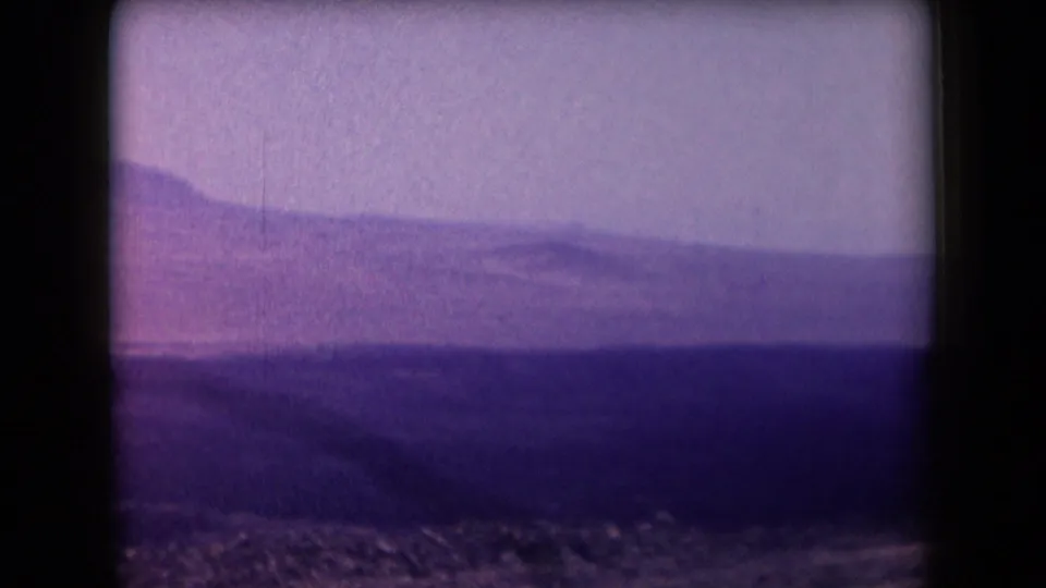 1958 Arizona aerial frame with layered hills, rocky terrain, and a hazy sky, viewed from a moving plane window.