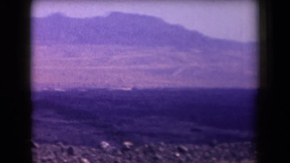 1958 Arizona desert view with a dark foreground band, distant ridgeline, hazy atmosphere, and visible 8mm frame borders.