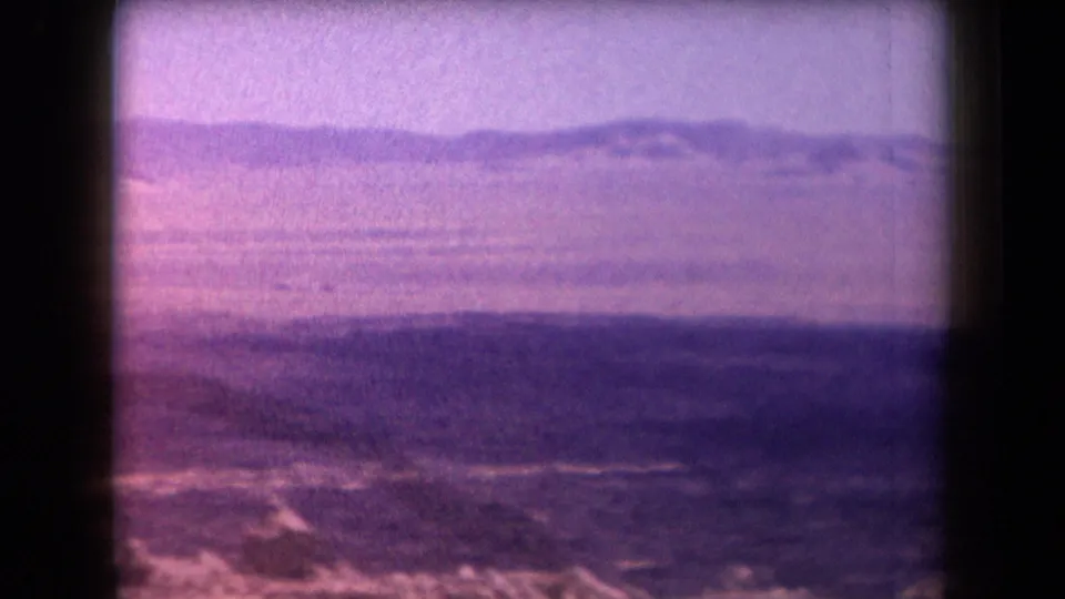 1958 Arizona desert frame with open terrain, low distant hills, rocky foreground texture, and a strong purple-magenta film shift.