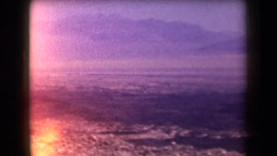 1958 Arizona home-movie still with distant hills, hazy open terrain, and dark window edges under a strong pink-purple film shift.