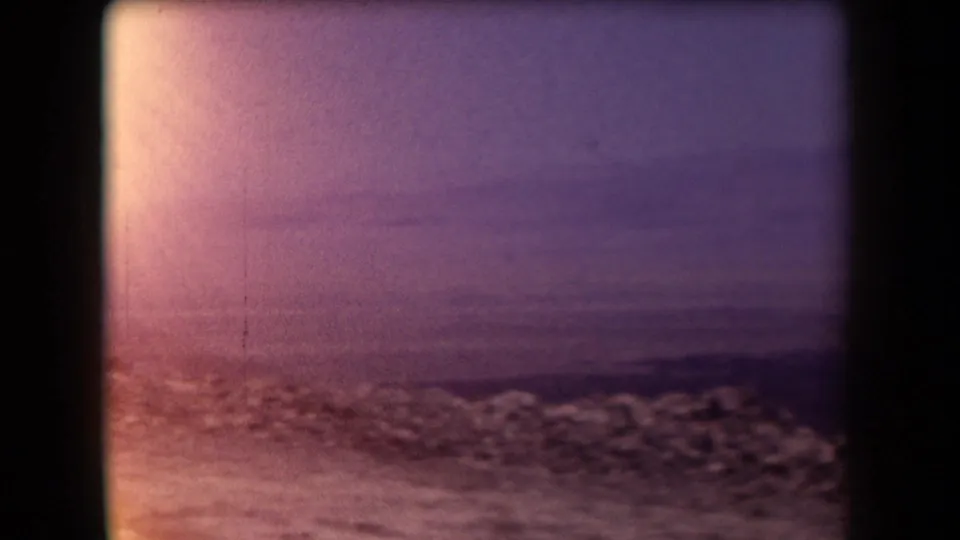 Final 1958 Arizona frame showing a soft, purple-tinted landscape through window edges, with rocky foreground and low mountains beyond.