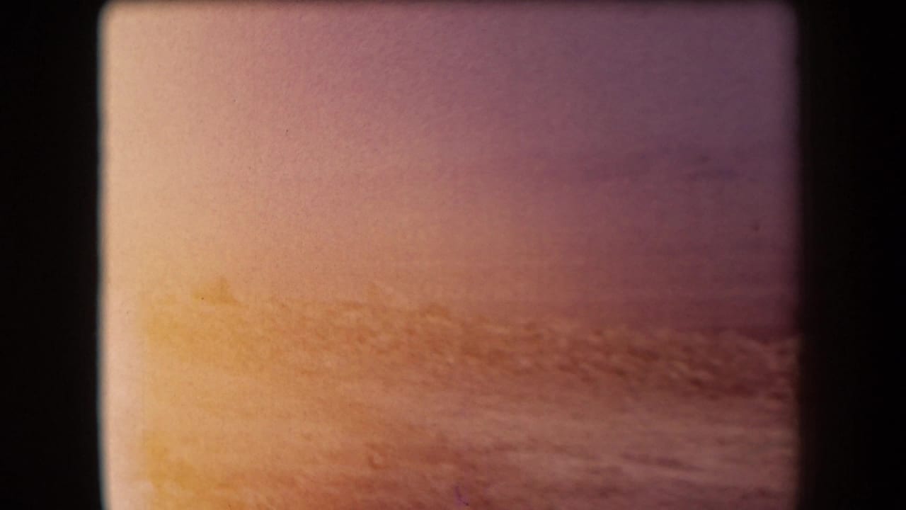 Faded 1958 8mm travel frame showing a warm horizon over water or flat landscape, bordered by dark film gate edges.