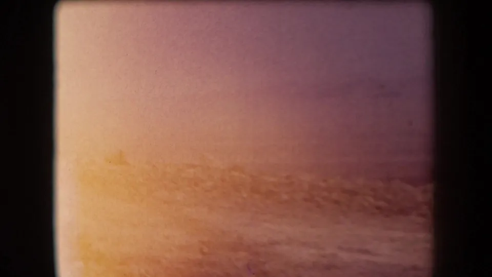 Faded 1958 8mm travel frame showing a warm horizon over water or flat landscape, bordered by dark film gate edges.