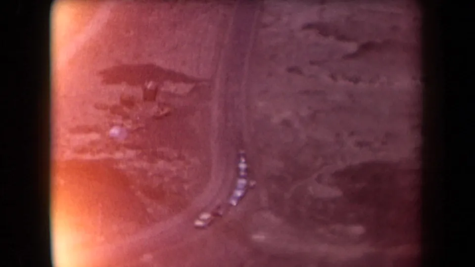 1958 Arizona 8mm frame showing a high view of a curving road in arid terrain, with small cars stopped or parked along the roadside.