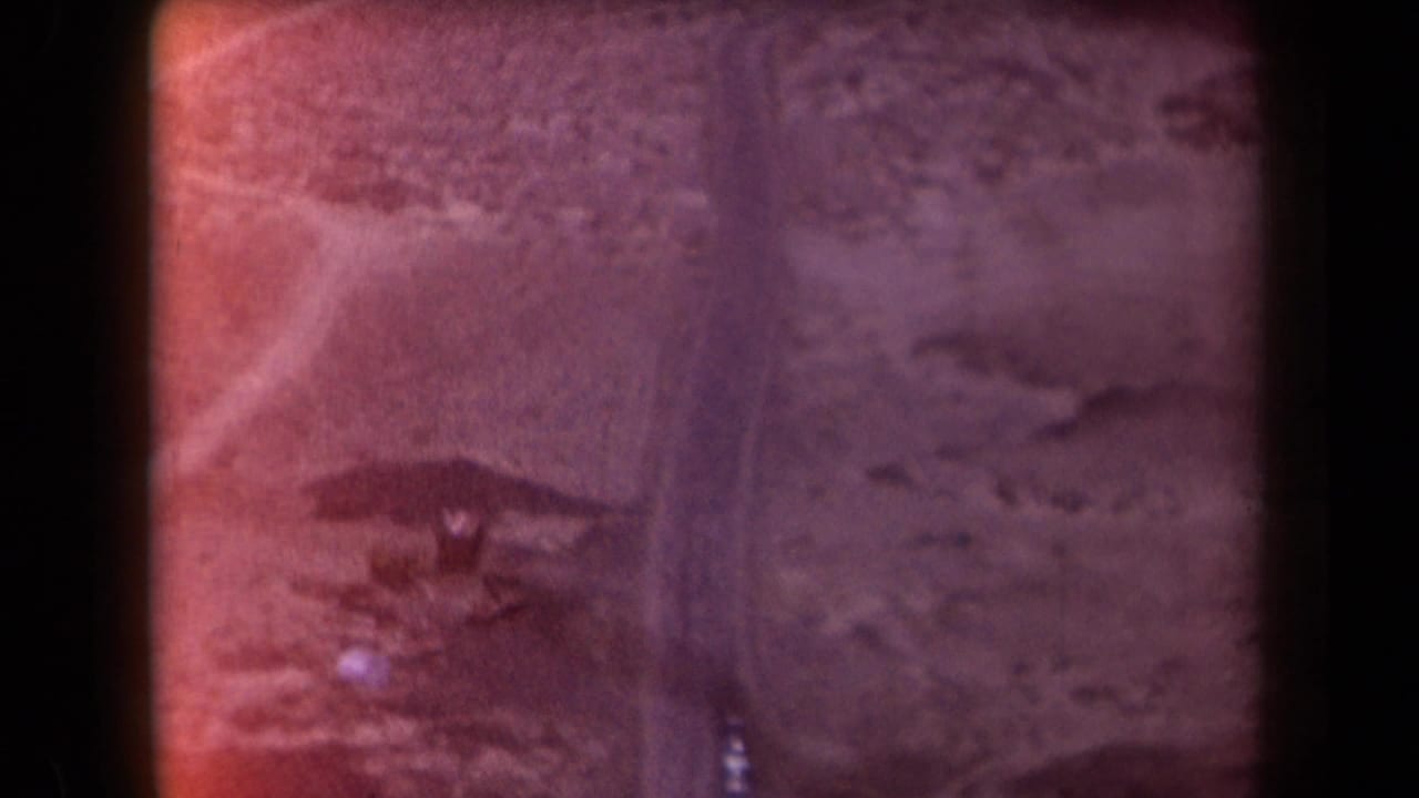 1958 Arizona 8mm frame showing rugged desert terrain, a winding road, and distant mountains under a hazy sky.
