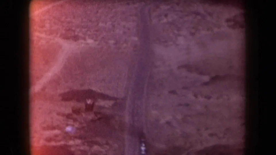 1958 Arizona 8mm frame showing rugged desert terrain, a winding road, and distant mountains under a hazy sky.
