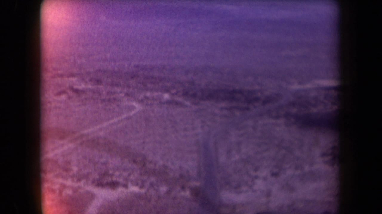 Aerial 1958 Arizona view of a pale road running through desert hills and distant mountain forms.