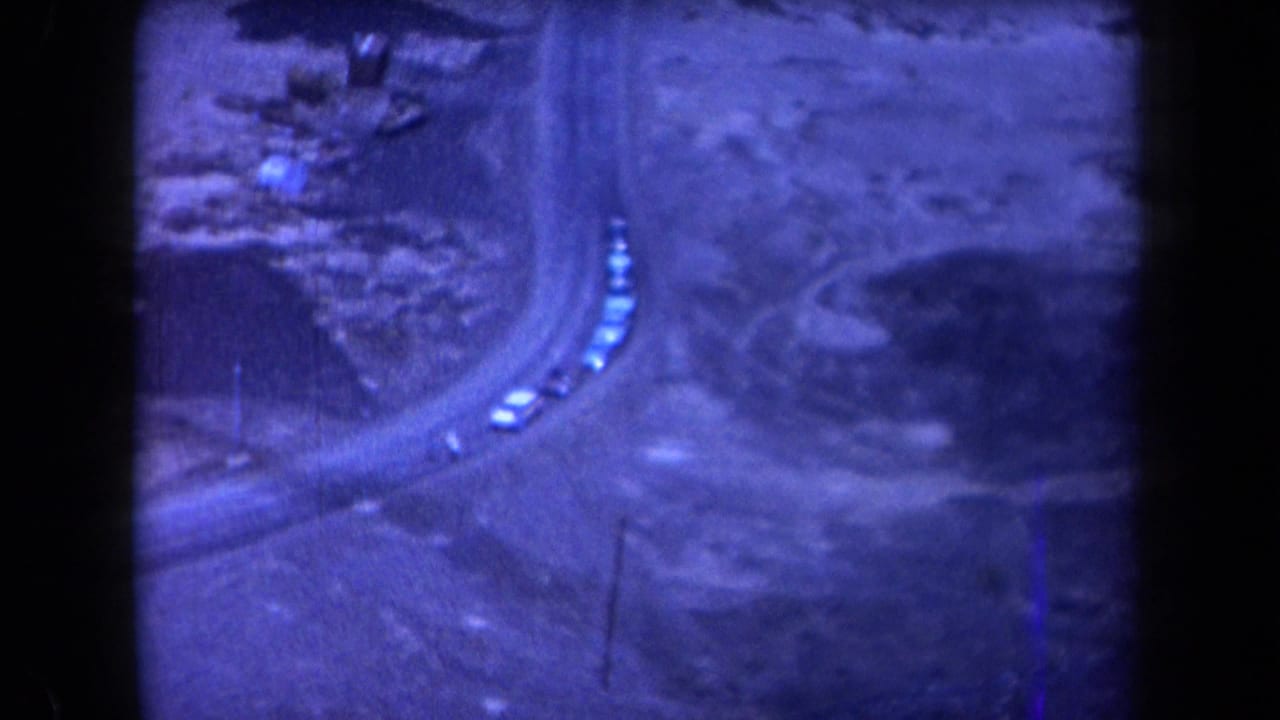 Cars continue along the curved road between rocky slopes and sparse desert vegetation.