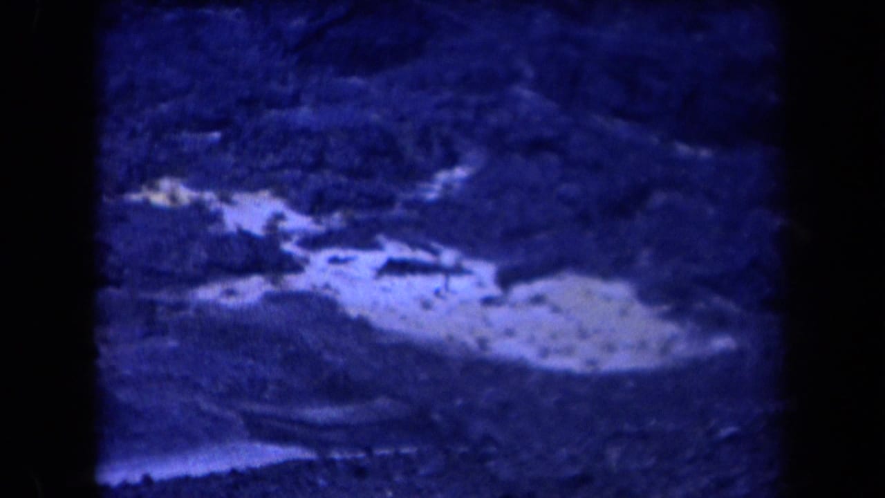 1958 Arizona home-movie frame showing rocky desert terrain under a deep blue cast, with no clear figure visible in this still.