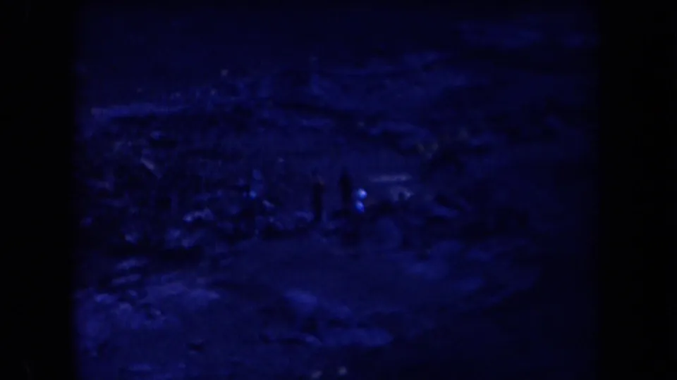 Blue-tinted 1958 Arizona 8mm frame showing a dim open landscape with small human figures and heavy film borders.