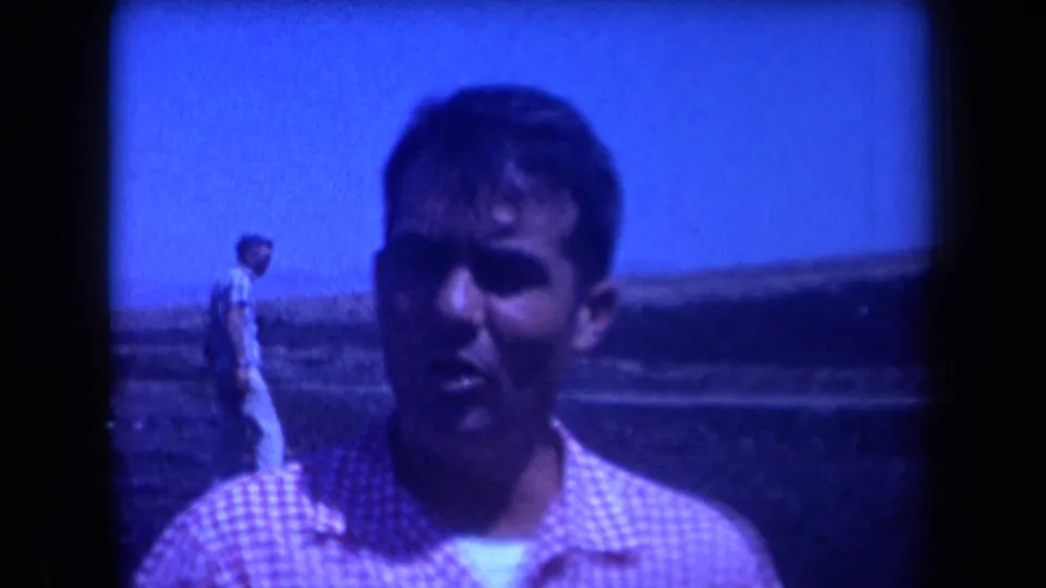 Adult man in a red-and-white checkered shirt faces the camera in a blue-tinted 1958 Arizona home-movie frame.