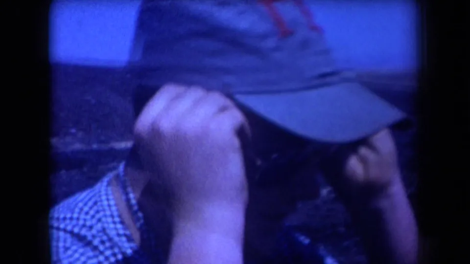 Close 1958 Arizona 8mm frame of an adult man in a checkered shirt holding a cap near his face under strong blue tint.
