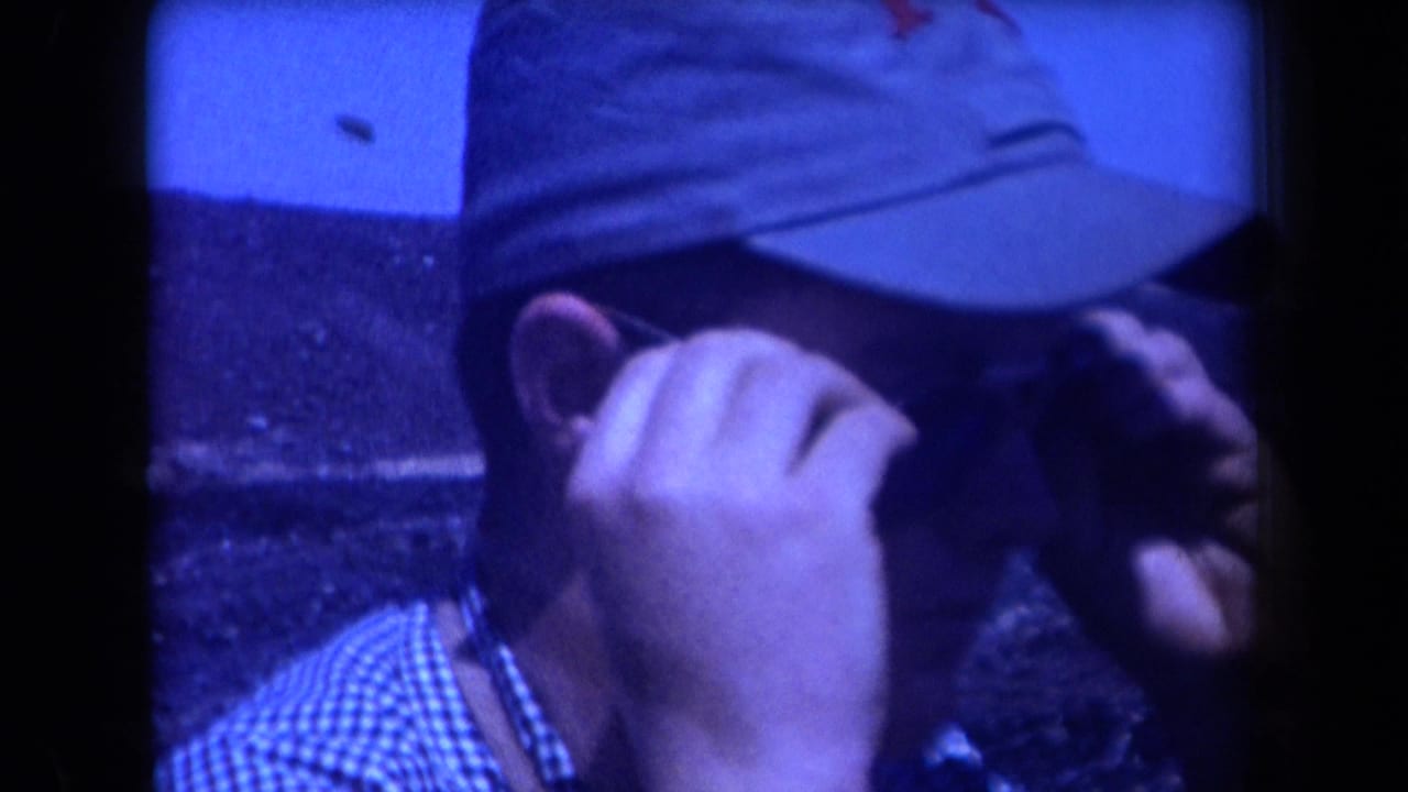In 1958 Arizona home-movie footage, a capped man in a checkered shirt adjusts his glasses beside a dark coal mound.